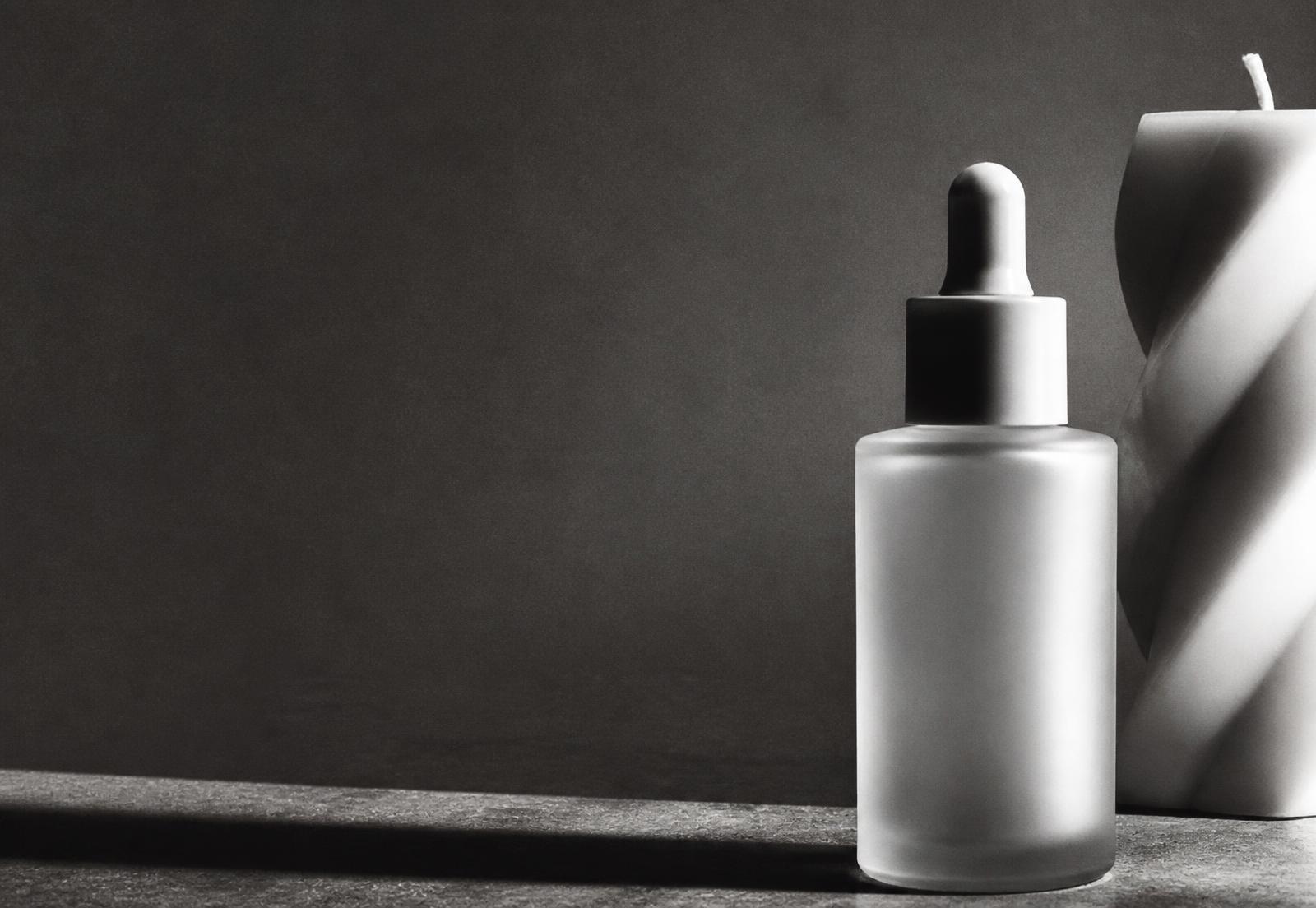 Unbranded frosted glass cosmetic bottle and sculptural candle in high-contrast black and white